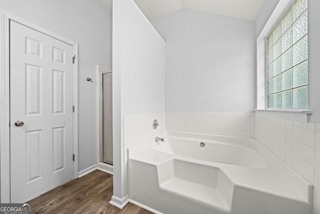 full bath featuring wood finished floors, a shower stall, a garden tub, lofted ceiling, and baseboards