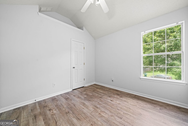 empty room with plenty of natural light, lofted ceiling, wood finished floors, ceiling fan, and baseboards
