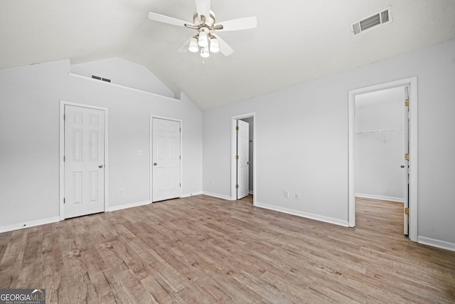 unfurnished bedroom with wood finished floors, vaulted ceiling, baseboards, a ceiling fan, and a spacious closet
