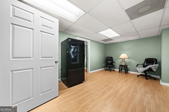 living area featuring light wood-style floors, baseboards, and a drop ceiling