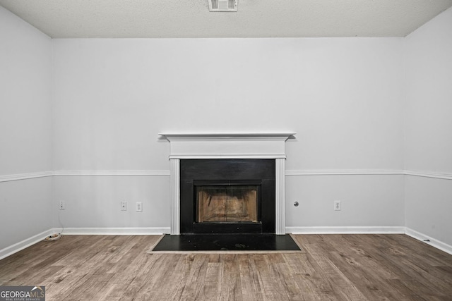 detailed view of wood finished floors, a fireplace with flush hearth, baseboards, and a textured ceiling