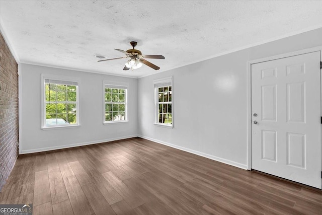 spare room with a textured ceiling, dark wood-type flooring, a ceiling fan, crown molding, and brick wall