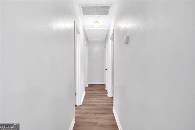 hall featuring attic access, baseboards, wood finished floors, and a textured ceiling