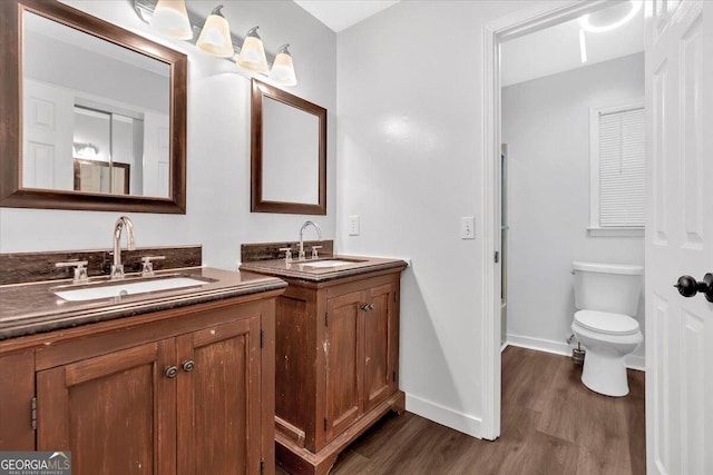 full bath with wood finished floors, two vanities, baseboards, and toilet