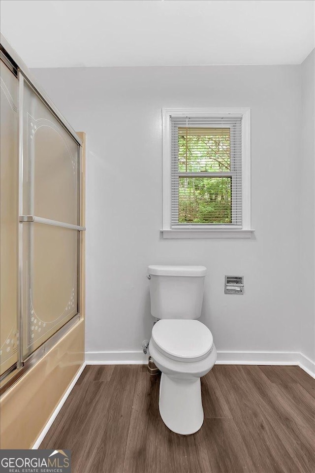 bathroom with baseboards, wood finished floors, toilet, and shower / bath combination with glass door