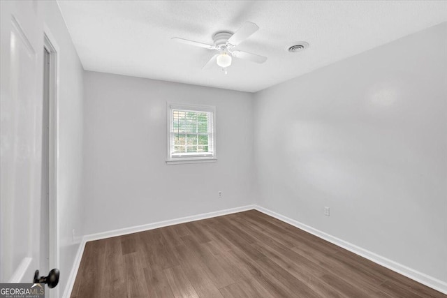 empty room featuring dark wood-style flooring, a ceiling fan, and baseboards