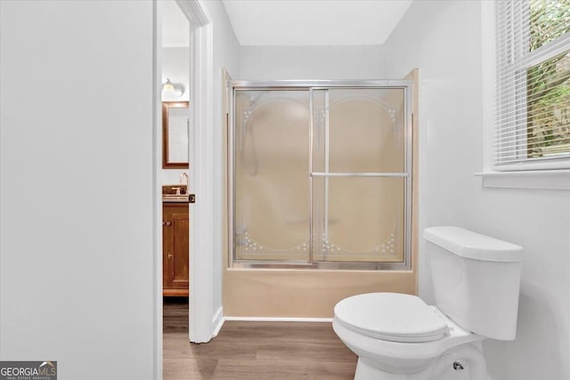 bathroom featuring wood finished floors, toilet, shower / bath combination with glass door, baseboards, and vanity