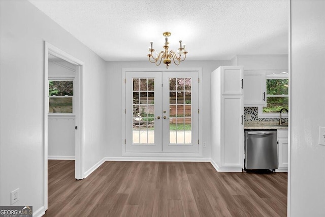 unfurnished dining area with dark wood-type flooring, a chandelier, a sink, baseboards, and a textured ceiling