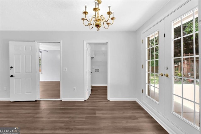 unfurnished dining area with a chandelier, baseboards, dark wood-style floors, and french doors