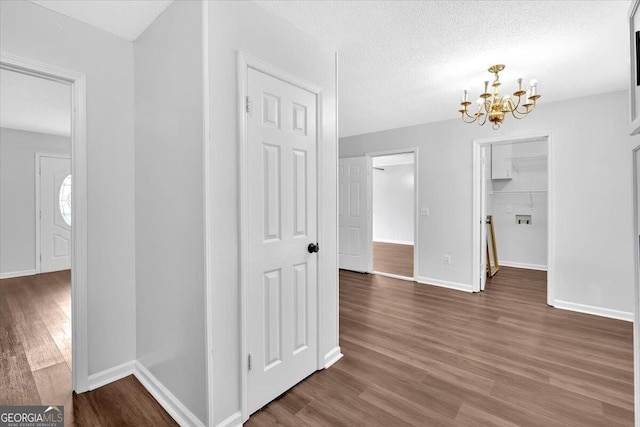 hallway featuring a chandelier, wood finished floors, baseboards, and a textured ceiling