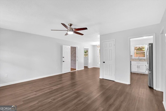 unfurnished living room featuring ceiling fan, dark wood finished floors, baseboards, and a sink