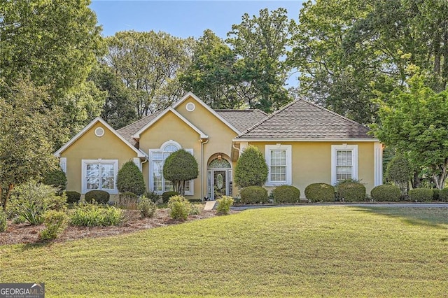 traditional-style house featuring stucco siding, a front lawn, and roof with shingles