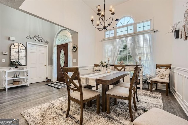 dining room featuring a chandelier, a decorative wall, high vaulted ceiling, wood finished floors, and wainscoting