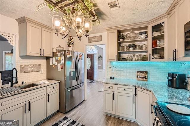 kitchen with stainless steel fridge, a textured ceiling, a sink, tasteful backsplash, and light wood finished floors