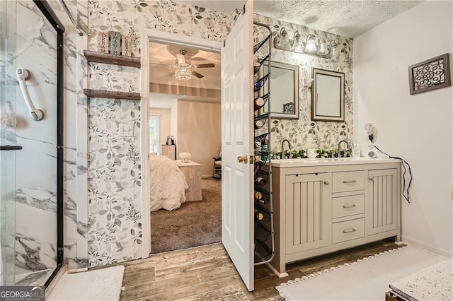 ensuite bathroom with wallpapered walls, a ceiling fan, a marble finish shower, a textured ceiling, and wood finished floors