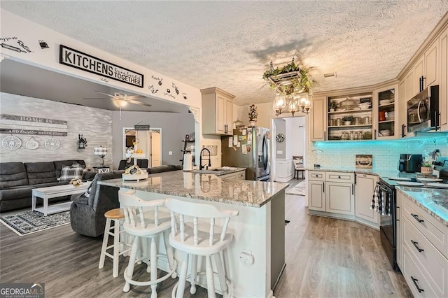 kitchen featuring stainless steel appliances, a sink, open floor plan, light wood-style flooring, and light stone countertops