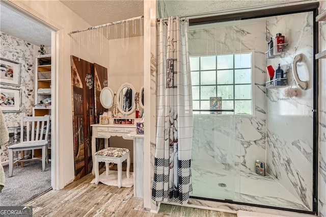 bathroom with a marble finish shower, wood finished floors, a textured ceiling, and wallpapered walls