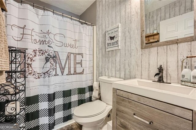 bathroom featuring wood walls, toilet, vanity, a textured ceiling, and a shower with shower curtain