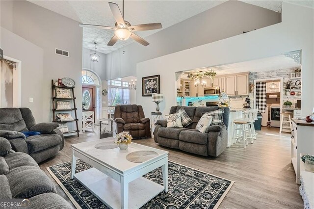 living room with a chandelier, high vaulted ceiling, ceiling fan, and light wood-type flooring