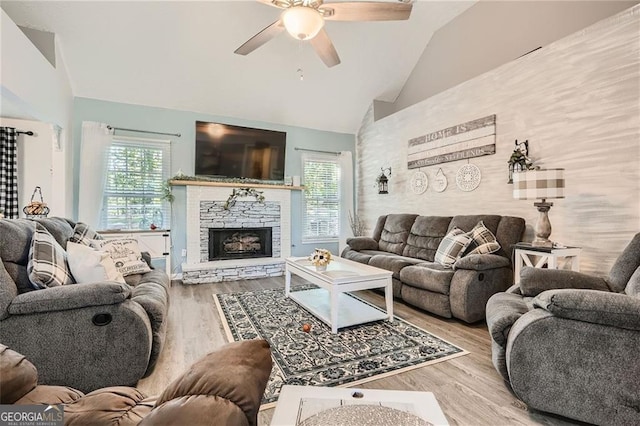 living area with vaulted ceiling, ceiling fan, wood finished floors, and a stone fireplace