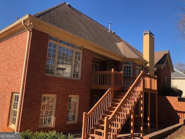 rear view of property with brick siding, a chimney, and stairs