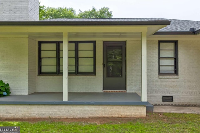 doorway to property featuring crawl space, brick siding, a porch, and a shingled roof