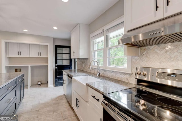 kitchen with stainless steel appliances, a sink, light stone countertops, white cabinetry, and backsplash