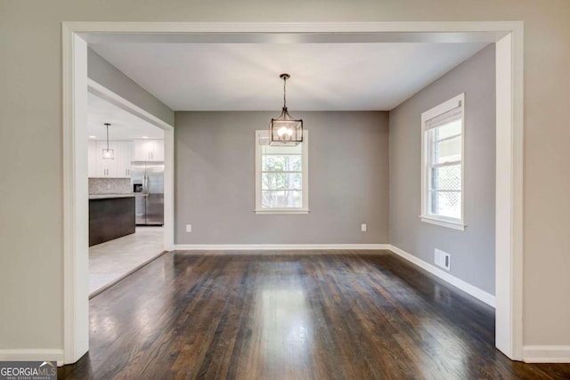unfurnished dining area featuring dark wood-style floors, plenty of natural light, baseboards, and a chandelier