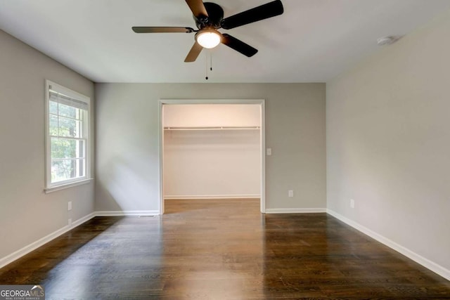 unfurnished bedroom featuring wood finished floors, baseboards, a spacious closet, and ceiling fan