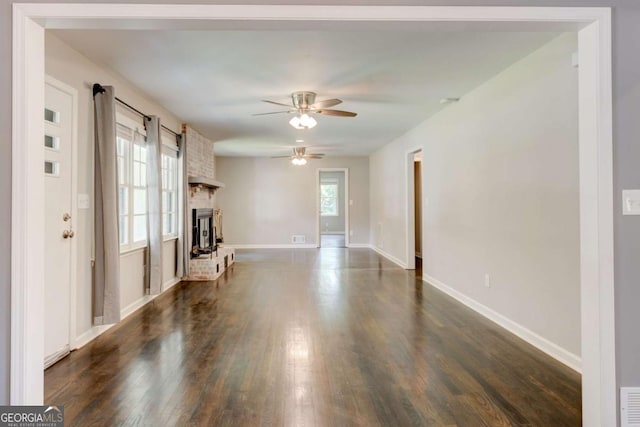 unfurnished living room with ceiling fan, dark wood-style floors, baseboards, and a brick fireplace