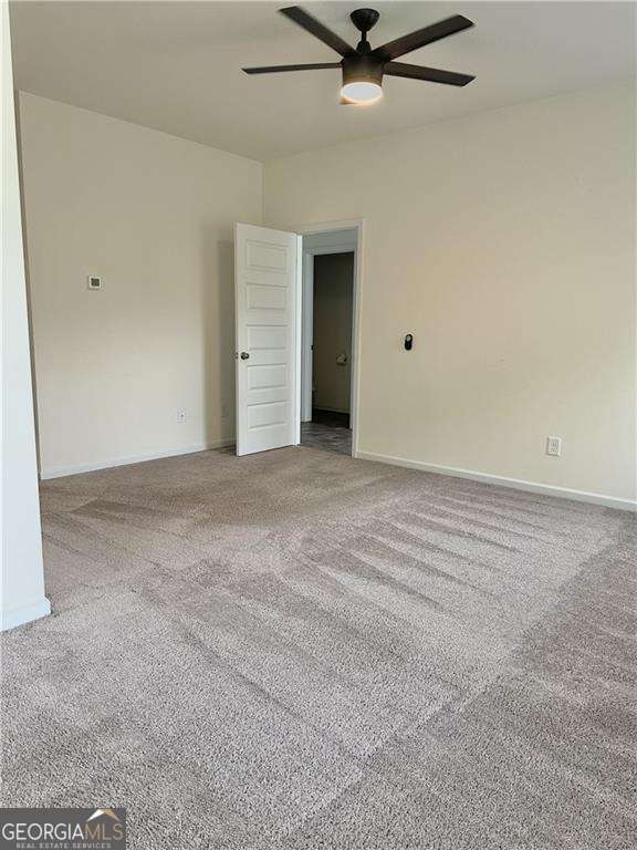 carpeted spare room with a ceiling fan and baseboards
