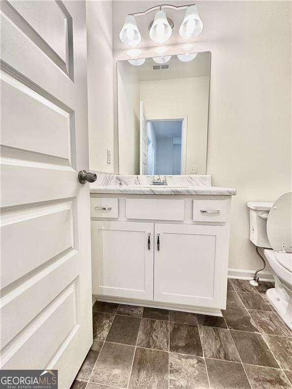 bathroom with toilet, vanity, baseboards, and stone finish floors