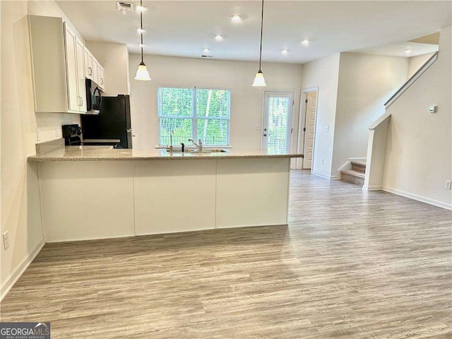 kitchen featuring light wood-style floors, black appliances, baseboards, a peninsula, and white cabinetry