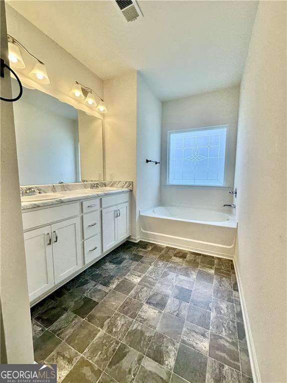 full bathroom with baseboards, double vanity, a garden tub, and stone finish flooring