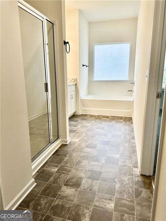 full bathroom featuring a stall shower, a bath, vanity, and baseboards
