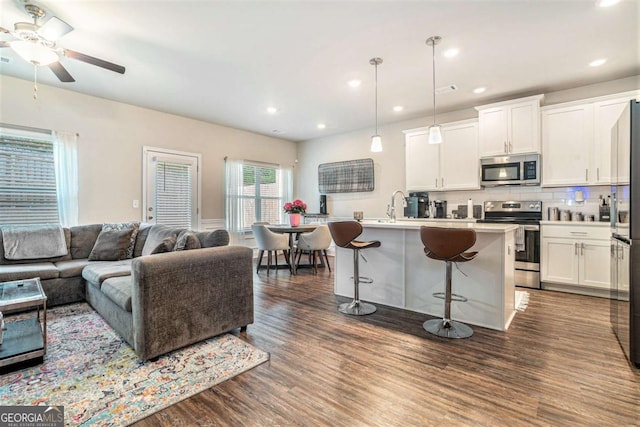450 Rockfern Ct, Lilburn, GA 30047 - kitchen with appliances with stainless steel finishes, open floor plan, dark wood-style flooring, white cabinetry, and a kitchen breakfast bar