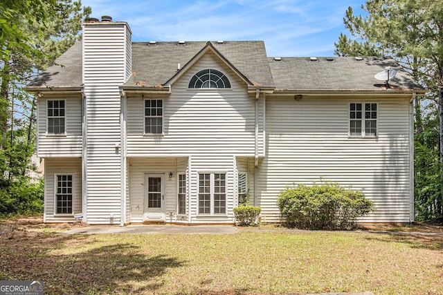 rear view of house featuring a yard, a chimney, a patio area, and a shingled roof