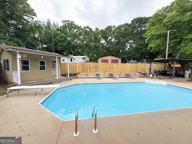 view of swimming pool featuring view of scattered trees, fence, a diving board, an outbuilding, and a patio