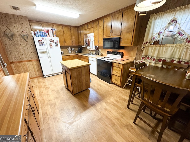 kitchen featuring white appliances, light countertops, light wood finished floors, a kitchen island, and wood walls
