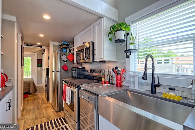 kitchen featuring appliances with stainless steel finishes, a sink, light wood-style flooring, white cabinets, and dark countertops