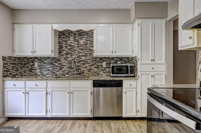 kitchen featuring stainless steel appliances, a sink, white cabinets, and light stone countertops