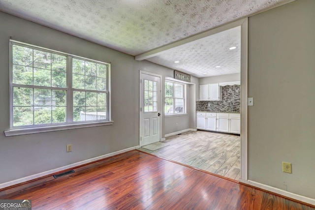 interior space with light wood finished floors, baseboards, white cabinets, backsplash, and recessed lighting