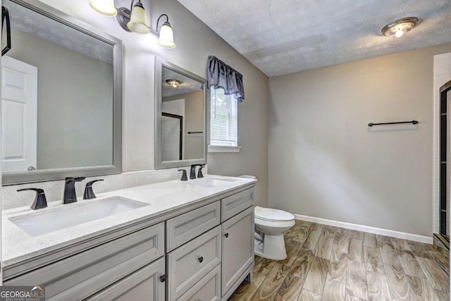 bathroom featuring a stall shower, a textured ceiling, wood finished floors, double vanity, and toilet