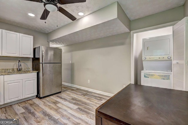 kitchen featuring freestanding refrigerator, stacked washer / dryer, a sink, white cabinetry, and light wood-type flooring