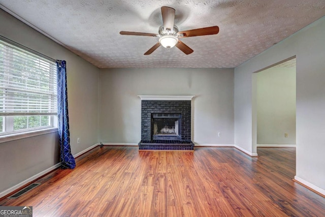 unfurnished living room featuring wood finished floors, ceiling fan, baseboards, a fireplace, and a textured ceiling