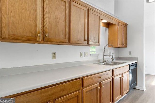 kitchen featuring a sink, black dishwasher, light countertops, light wood-style floors, and baseboards