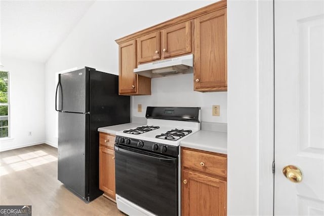 kitchen featuring under cabinet range hood, gas range oven, lofted ceiling, light countertops, and freestanding refrigerator