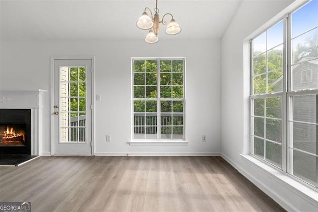 unfurnished living room with wood finished floors, healthy amount of natural light, and a warm lit fireplace
