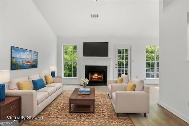 living room featuring a warm lit fireplace, wood finished floors, baseboards, and high vaulted ceiling
