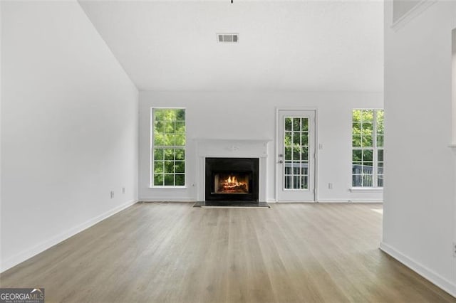 unfurnished living room featuring a fireplace with flush hearth, wood finished floors, baseboards, and vaulted ceiling